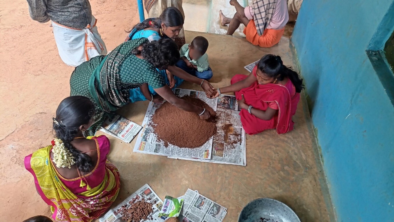 Khushboo, sits in the centre of the image in a red saree, examining soil samples