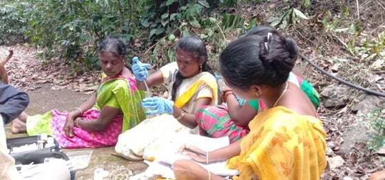 khushboo, wearing blue gloves and holding a testtube, is joined by other community members on a field visit